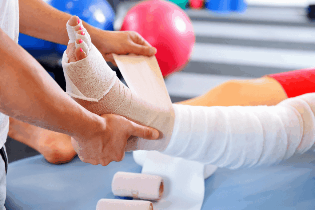 A person wraps a bandage around anothers foot and lower leg, already covered in white bandages—often seen in care routines for conditions like lymphedema. What is the Most Effective Treatment for Lymphedema? A gym ball and workout mat are visible in the background.