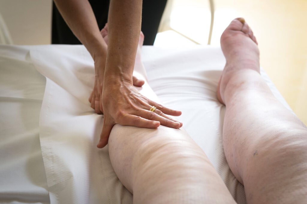 A person receives a therapeutic leg massage while lying on a white sheet-covered surface. Two hands gently press the lower thigh, focusing on relaxation and care—an important step in learning how to prevent lymphedema in legs and reduce your risk.