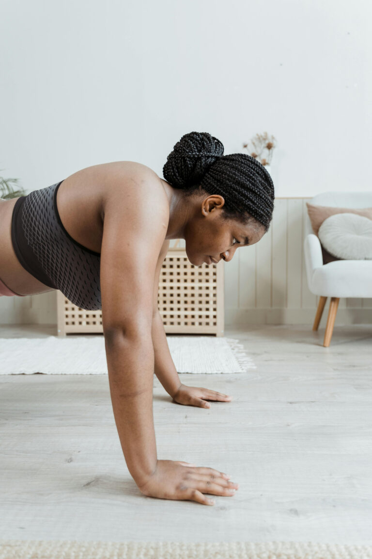 woman in a plank position on the gray floor wearing a black sports bra and black hair with braids