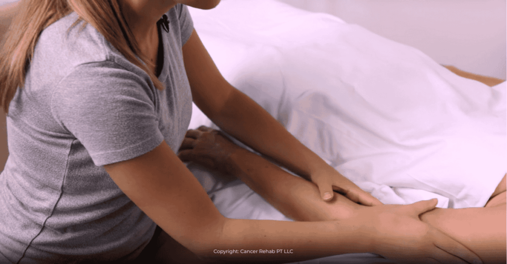 A physical therapist in a gray shirt gently massages the arm of another lying under a white blanket, performing manual lymphatic drainage—possibly following a guide to lymphedema treatment for managing arm lymphedema.