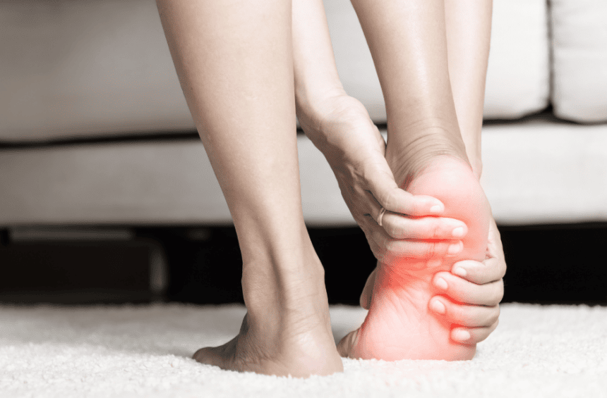 A person sitting and holding their foot with both hands, highlighting foot pain for neuropathy in the sole with a red glow effect around the toes and ball of the foot.