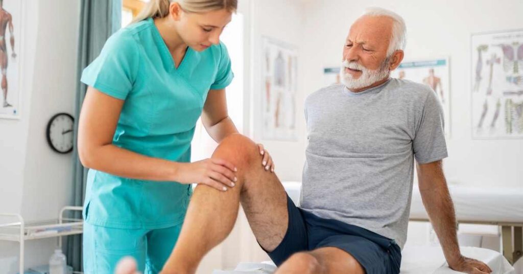 A healthcare professional examines an elderly man's knee in a medical office, checking for ways to reduce fluid for knee swelling as the man watches during the gentle assessment.
