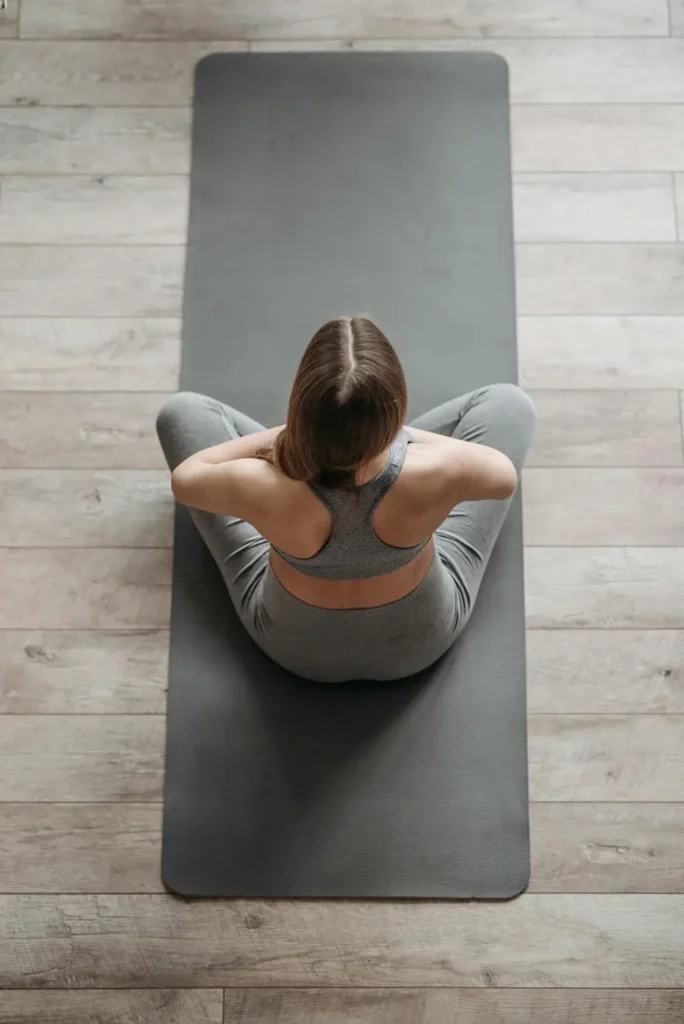 woman with brown hair, wearing gray sports bra and leggings, sitting on gray yoga mat
