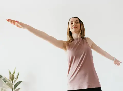 woman in pink shirt doing a yoga pose with her arms extended out