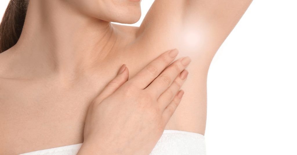 A woman with smooth skin smiles as she touches her armpit, which is highlighted with a soft glow—for those concerned about swelling under the armpit. She wears a white towel against a plain white background.