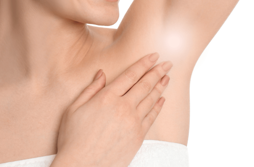 A woman with smooth skin smiles as she touches her armpit, which is highlighted with a soft glow—for those concerned about swelling under the armpit. She wears a white towel against a plain white background.