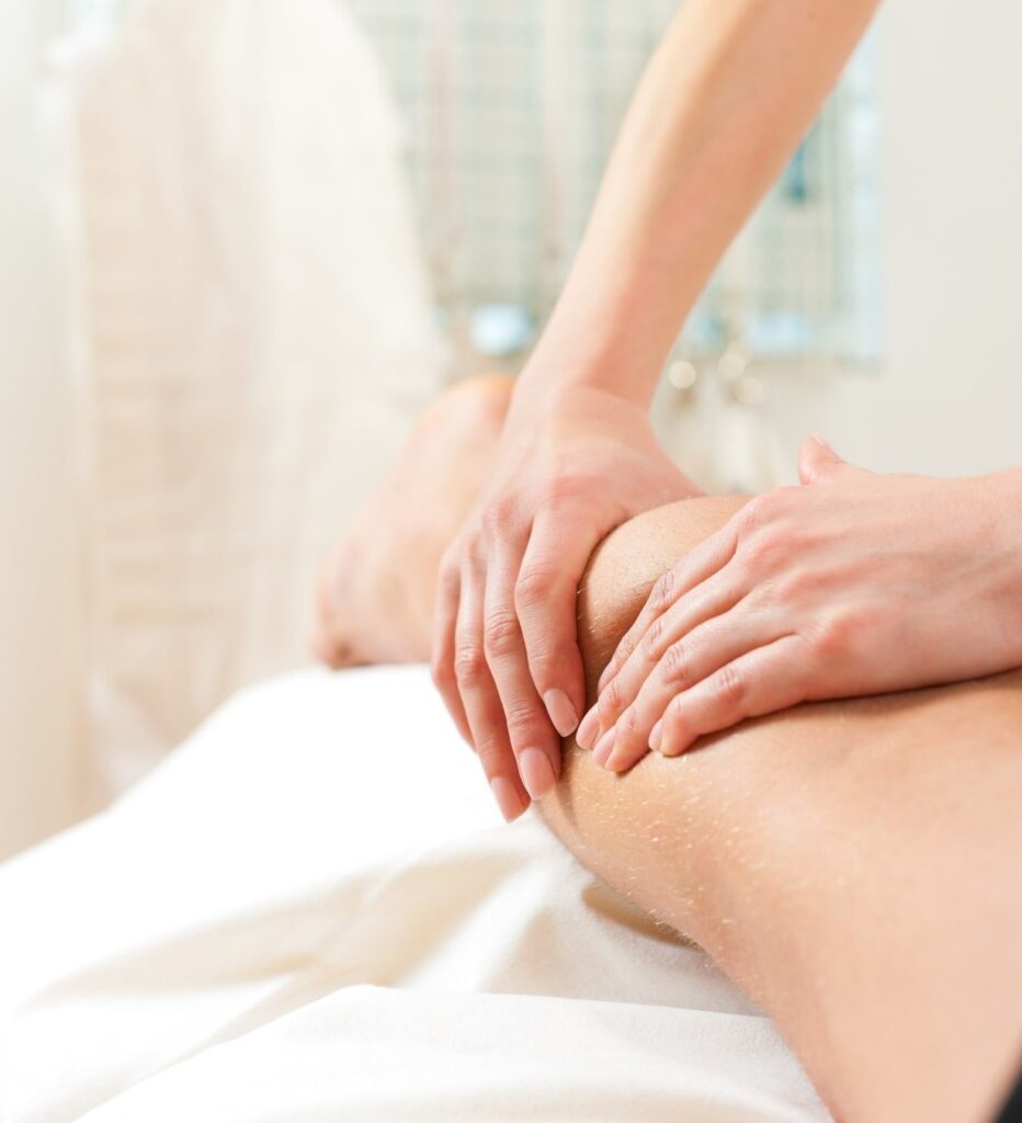 A close-up of a person receiving lymphedema treatment on their leg from a physical therapist, with both hands applying gentle pressure. The softly blurred background enhances the relaxing atmosphere.