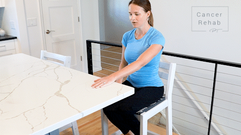 animated clip of a physical therapist sitting on a chair at a counter top, left arm on the table in front and leaning forward to show a shoulder stretch