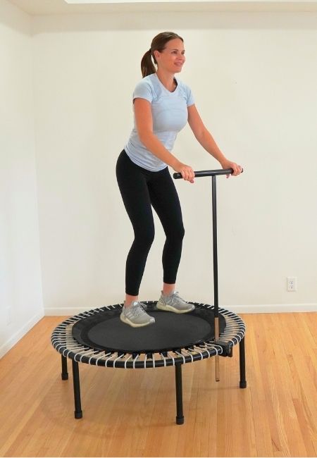 Kelly Sturm, physical therapist, in blue shirt and black pants jumping on a rebounder and holding onto handle