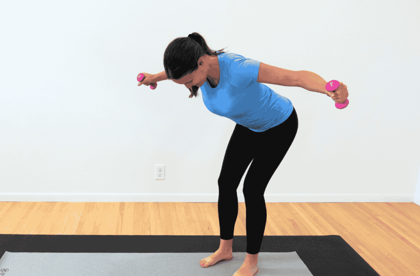 physical therapist in blue shirt and black pants on gray yoga mat, standing bent over with arms out to the side, hold smalling, yellow dumbbells showing exercise for breast cancer survivors