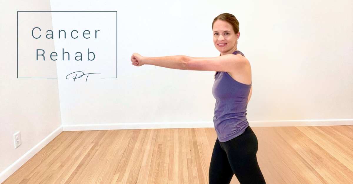 A woman standing with her right arm punched out in front of her, as she smiles at the camera.