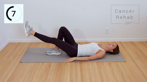 A certified lymphedema therapist lying on her back. She is raising her right leg up in the air and making small circles with her leg. 
