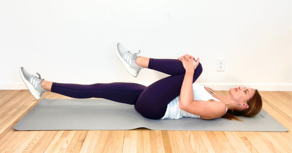 A certified lymphedema therapist lying on her back, hugging her left knee into her chest.