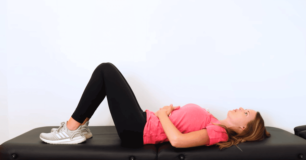 A woman lying on her back with her knees bent. Her hands are placed on her abdomen and she is taking a deep breath in and exhaling out.