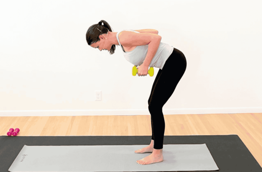 physical therapist in workout clothes, standing bent over on a yoga mat. Holding yellow dumbbells and rowing them up to her sides to show exercise after breast cancer radiation