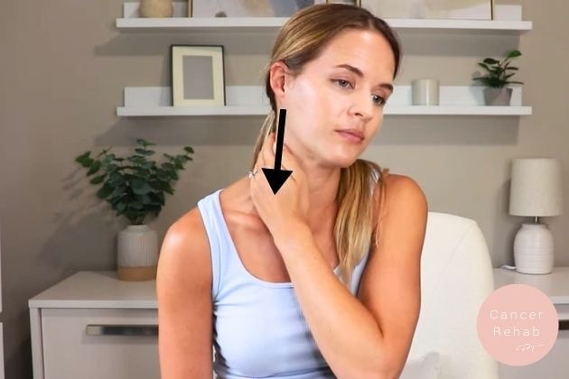 A woman sitting in a chair with her left hand massaging the lymph nodes in her neck.