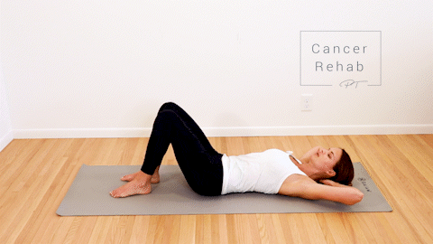 A certified lymphedema therapist lying on her back with knees bent and feet on the floor. She is gently twisting her trunk and knees from one side to the other.