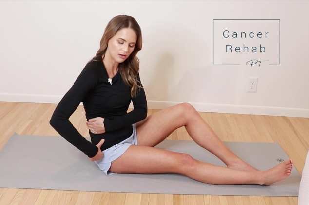 A certified lymphedema therapist sitting on a mat and massaging her torso as part of a manual lymphatic drainage routine.