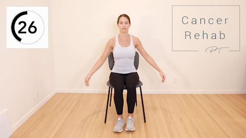 A woman sitting in a chair. She is lifting her leg and reaching with the opposite arm to tap her toe.