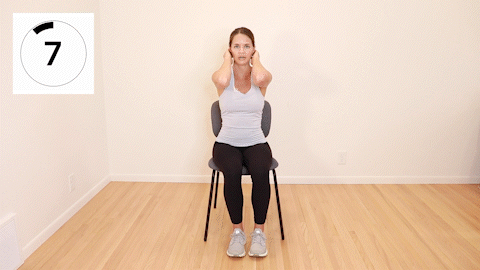 A woman sitting in a chair with her hands behind her head. She is slowly opening and closing her elbows.