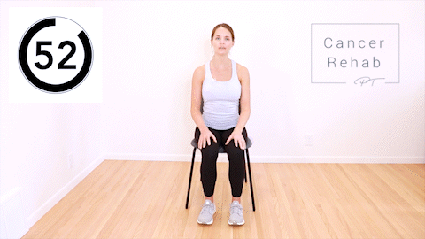 A woman sitting in a chair and extending her arm overhead as she bends to the opposite side.