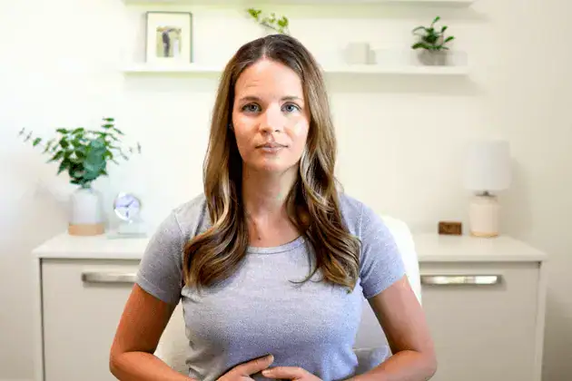 A woman in a seated position placing her hands gently on her belly and applying light pressure.