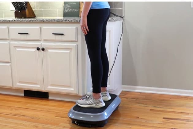 A woman standing on a vibration plate in a neutral position. 