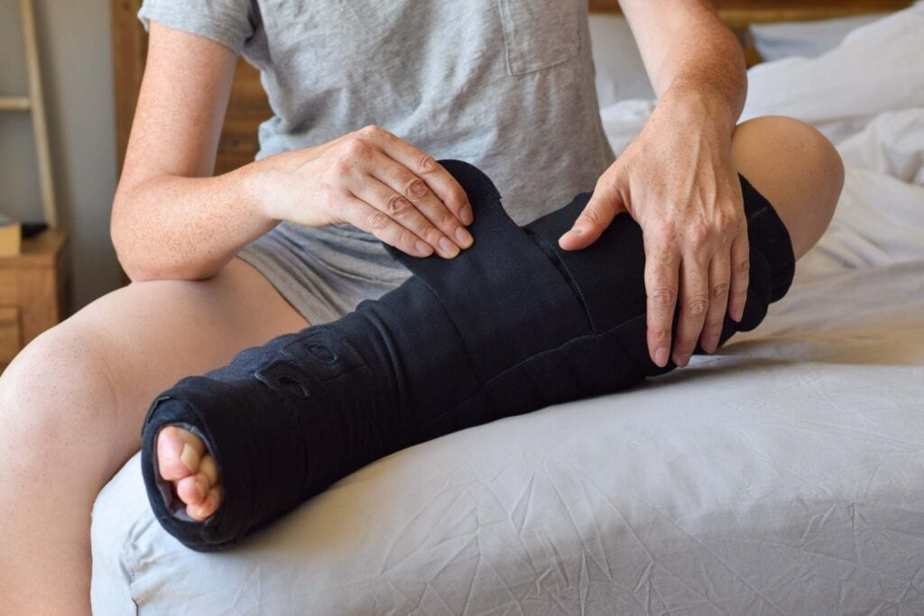 individual sitting on bed putting on black night compression garment to left lower leg